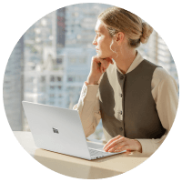 woman in suit sitting at a desk with surface device looking out of office window