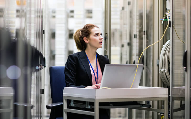 Woman on laptop in server room data center