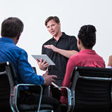 man standing, holding tablet, teaching clients