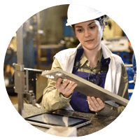 Hard hatted woman studying manufactured item with her tablet open.