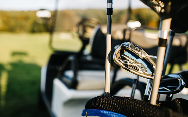Golf clubs drivers over green field background. Summer sunset