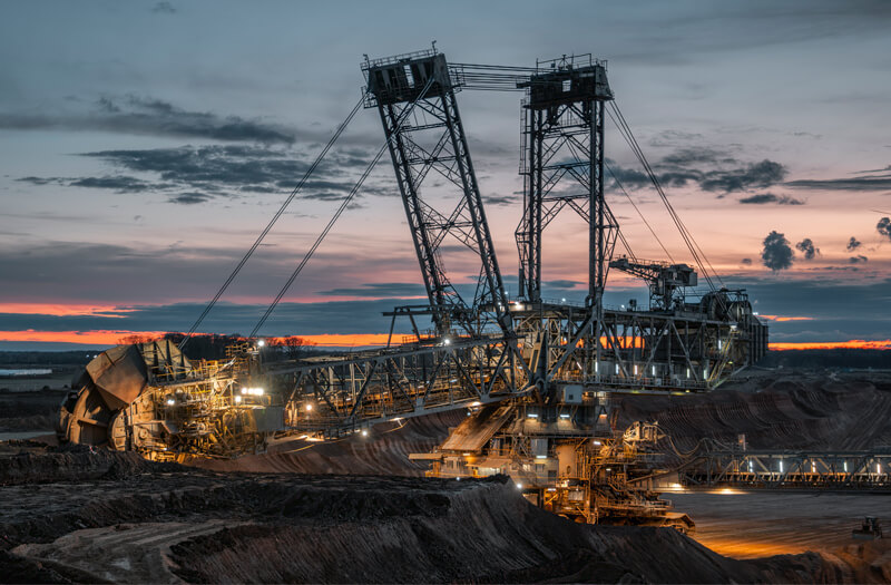 Bucket wheel excavator in a lignite open-pit mine at sunset, dramatic sky and exposed earth layers.