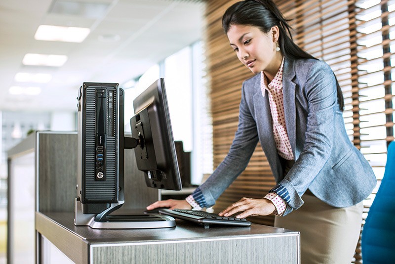 Receptionist leaning over front desk using the HP ProDesk 400 SFF G1 on IWC stand