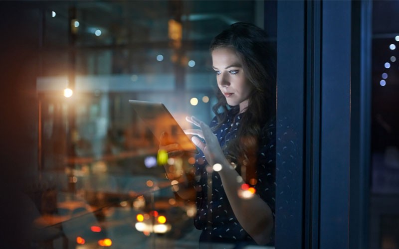 Woman using touch screen device in open office late at night