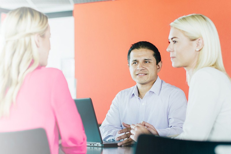 Three business people talking together while seated at table.