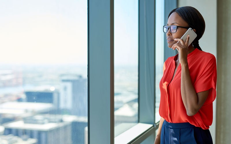 Woman looking out building window holding mobile phone