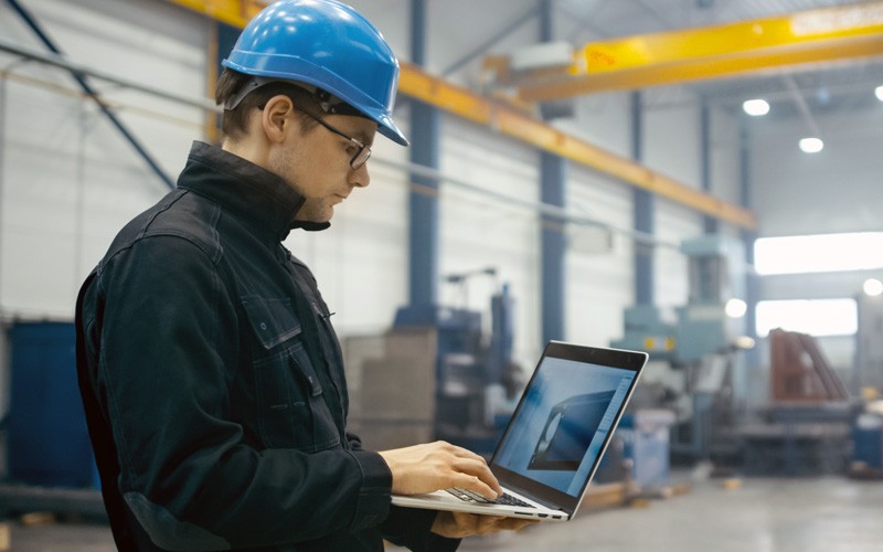 Man in hard hat on laptop in warehouse