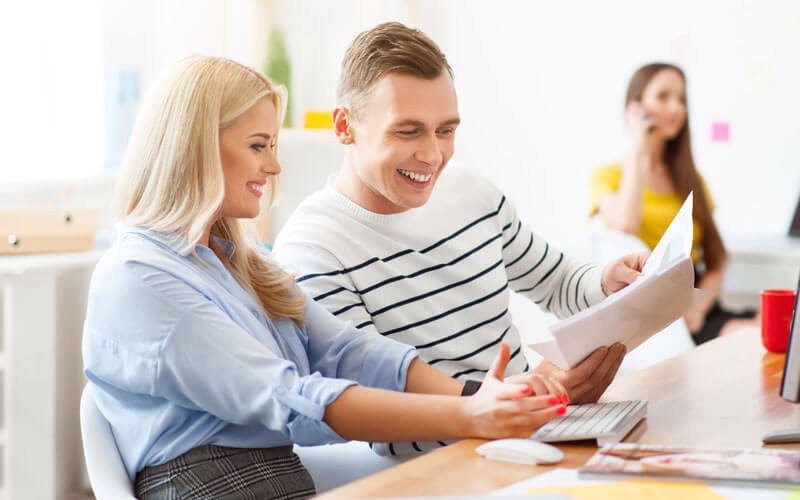 Two employees smiling looking at printed document