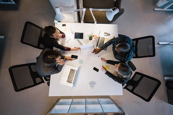 Team collaborates around table with smart devices, tablets and notebook computers