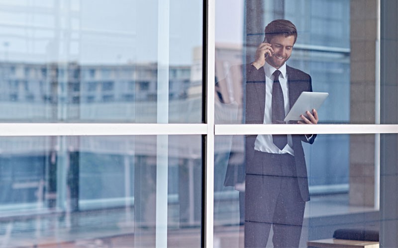 business-man-on-phone-holding-laptop-through-business-window