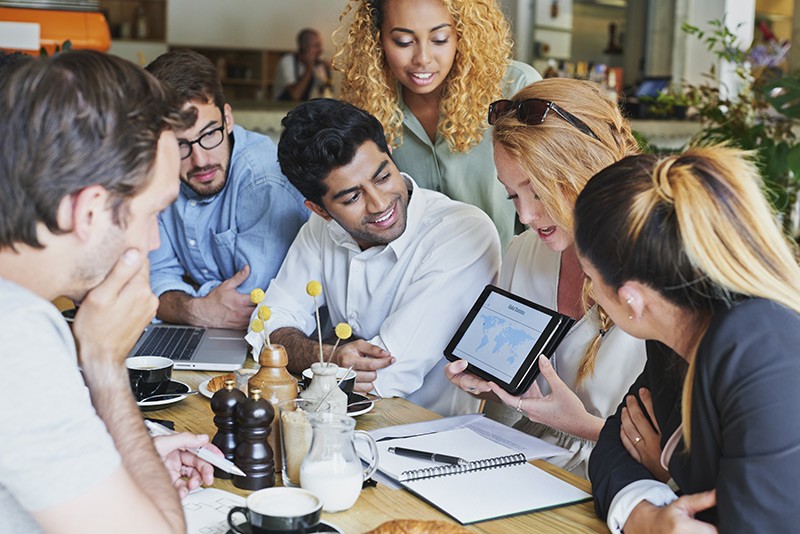 Team meets in a cafe to discuss project using multiple mobile devices