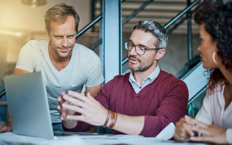 Three business professionals discuss over laptop device