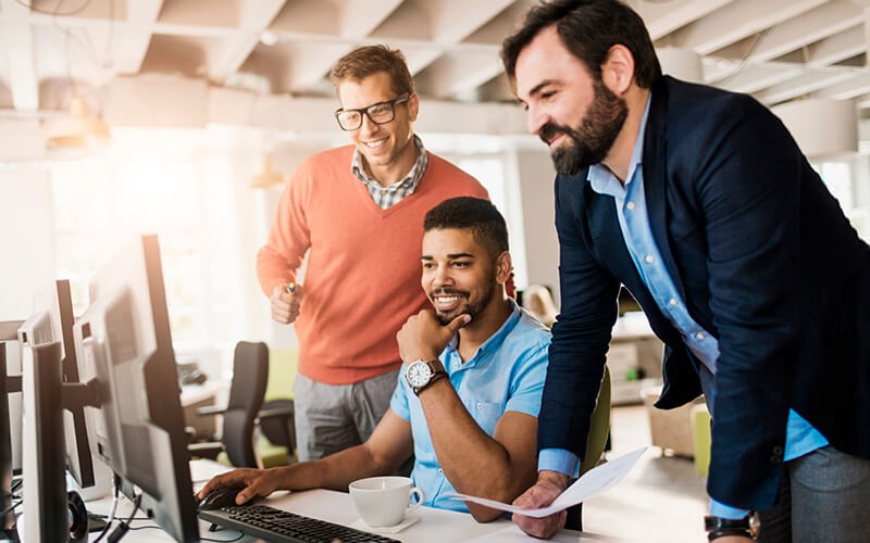 Group of smiling businessmen working in open office on desktop computer