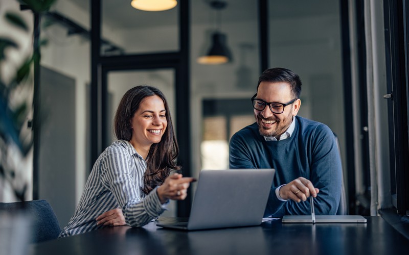 Utilisateurs collaborant en souriant dans la salle de réunion du bureau, sur l’ordinateur portable.