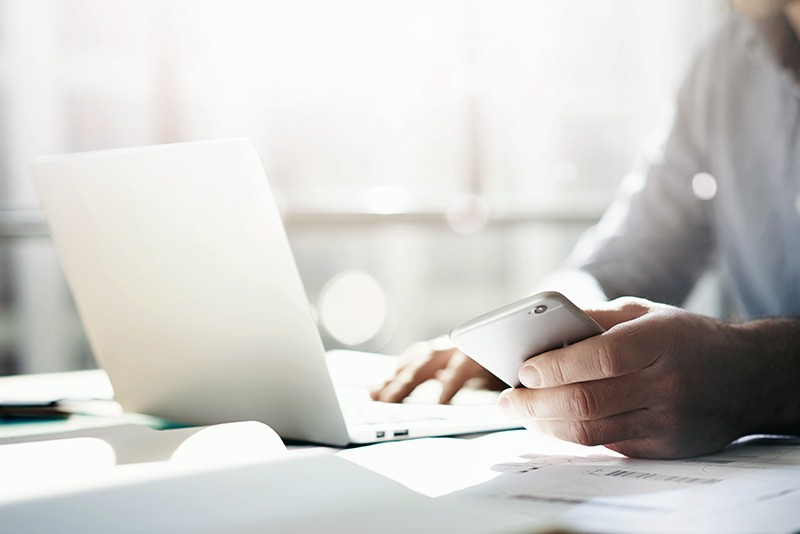Business professional using smart phone while at notebook computer