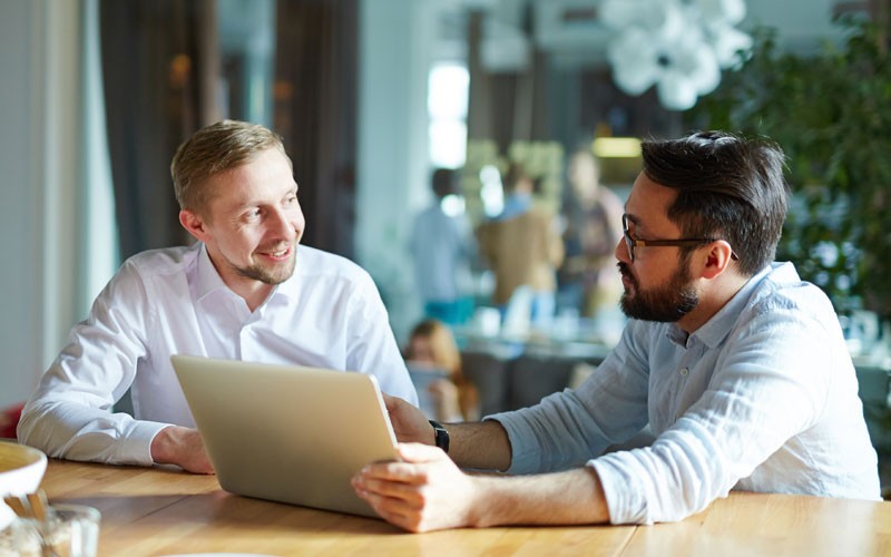 Two smiling businessmen discuss investments over tablet device